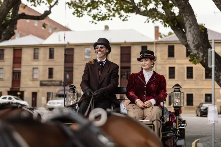 Dressed in the appropriate attire of the Golden Age, workers sit at the front of a horse-drawn carriage, ready to offer scenic rides to visitors at Battery Point, Hobart, Australia.