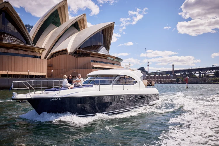 A family enjoying a private luxury yacht experience, cruising past the iconic Sydney Opera House with the city skyline in the background on a sunny day in Sydney, Australia.