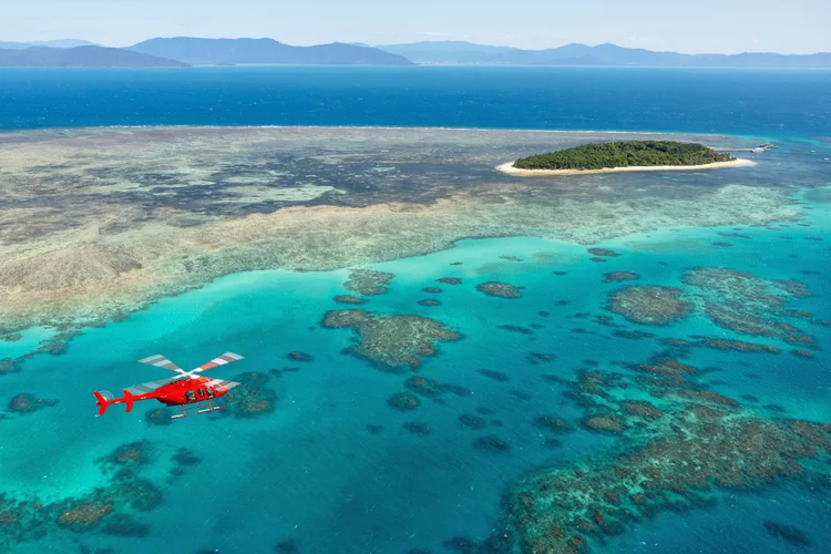 A couple riding in a private helicopter over the Great Barrier Reef in Cairns, Queensland, admiring the turquoise waters and coral formations below.
