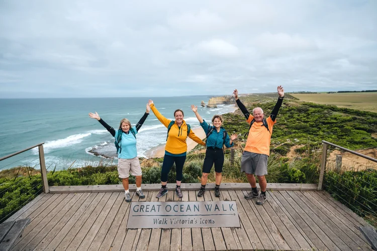 Four hikers stand together at a breathtaking lookout on the Twelve Apostles Signature Walk near Princetown on the Great Ocean Road in Australia.