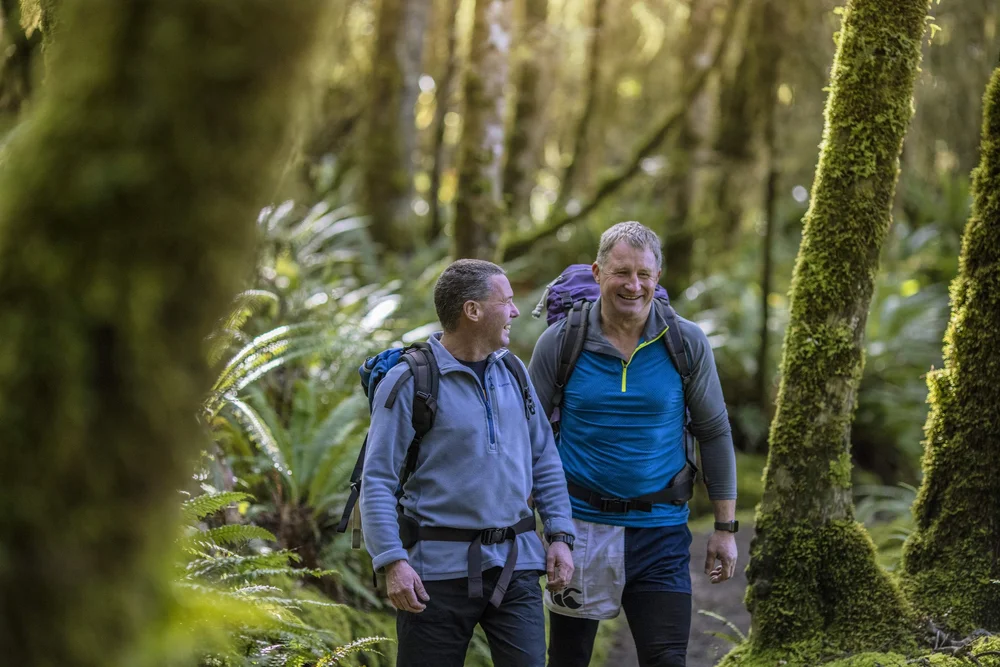 Two elderly men walking through the lush forest of the Kepler Track in Fiordland, New Zealand.