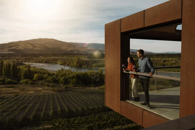 A couple sipping wine at a winery overlooking the vineyard in Central Otago, New Zealand.