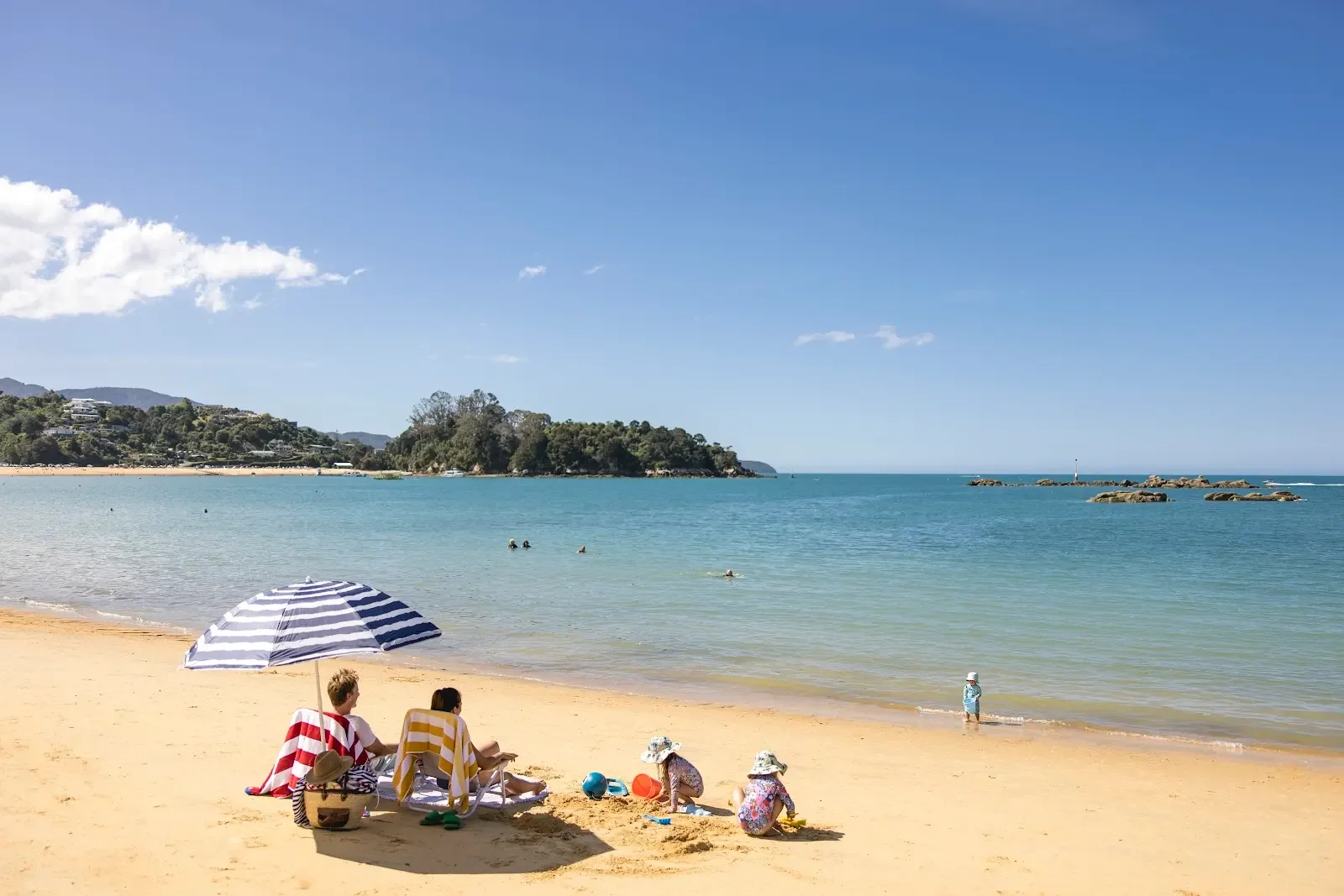 A family enjoying a sunny day on the sandy beach in Kaiteriteri, Nelson Tasman, playing by the shore with gentle waves and golden sand around them.