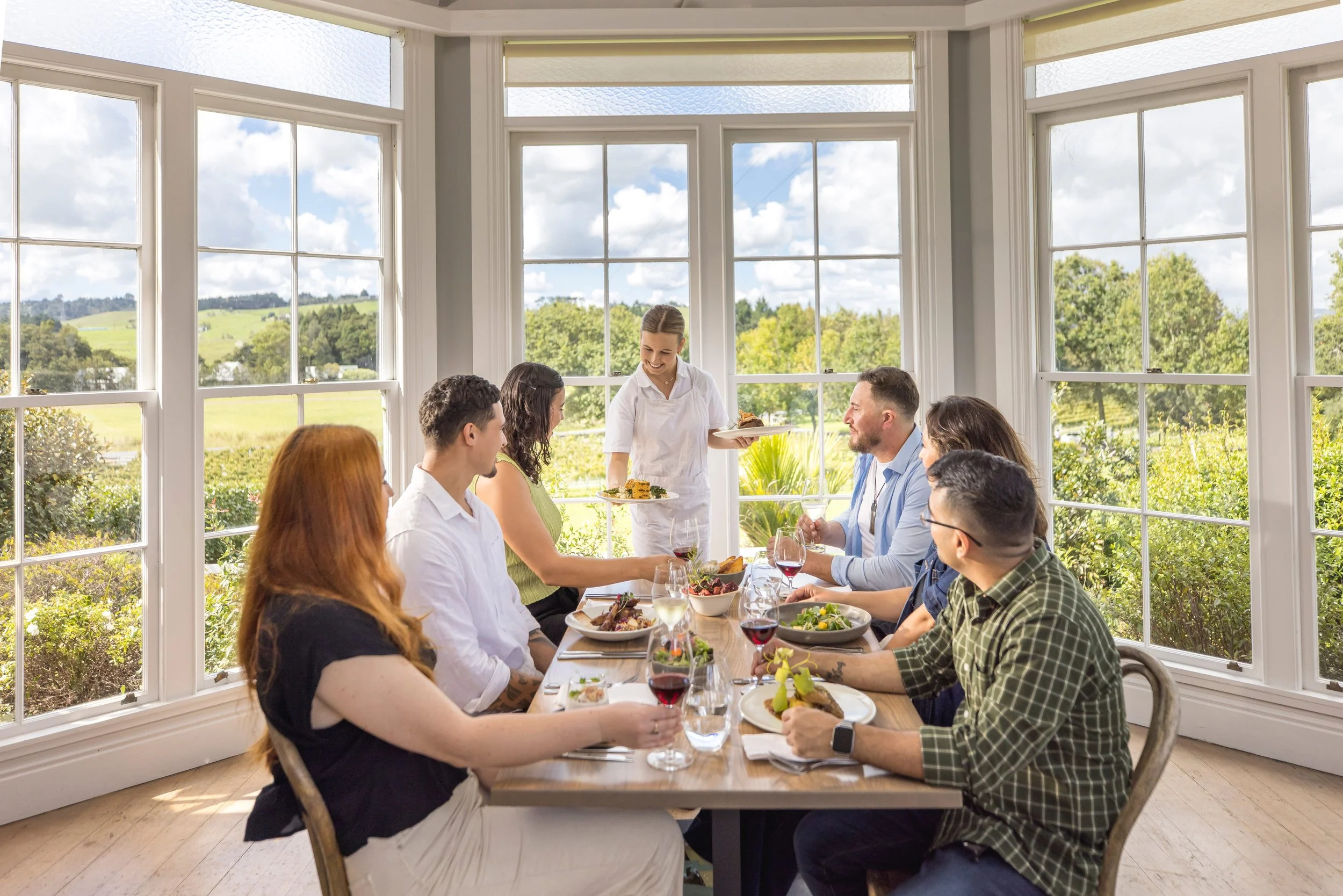 A group of couples enjoying a private luxury dining experience outdoors in Waimauku, Auckland, surrounded by elegant table settings.