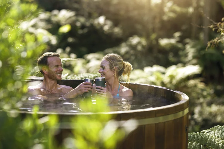 A couple sitting in the Secret Spot Hot Tubs in Rotorua, Bay of Plenty, New Zealand, with green foliage surrounding them.