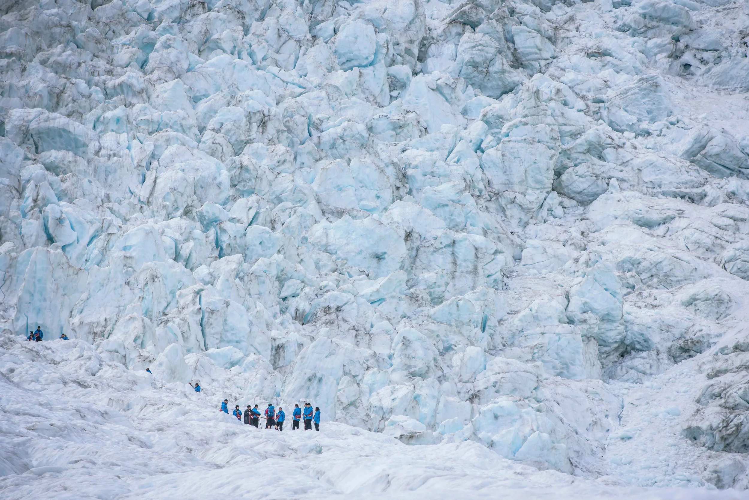 A group of hikers makes their way across the icy blue terrain of the Franz Josef Glacier in New Zealand