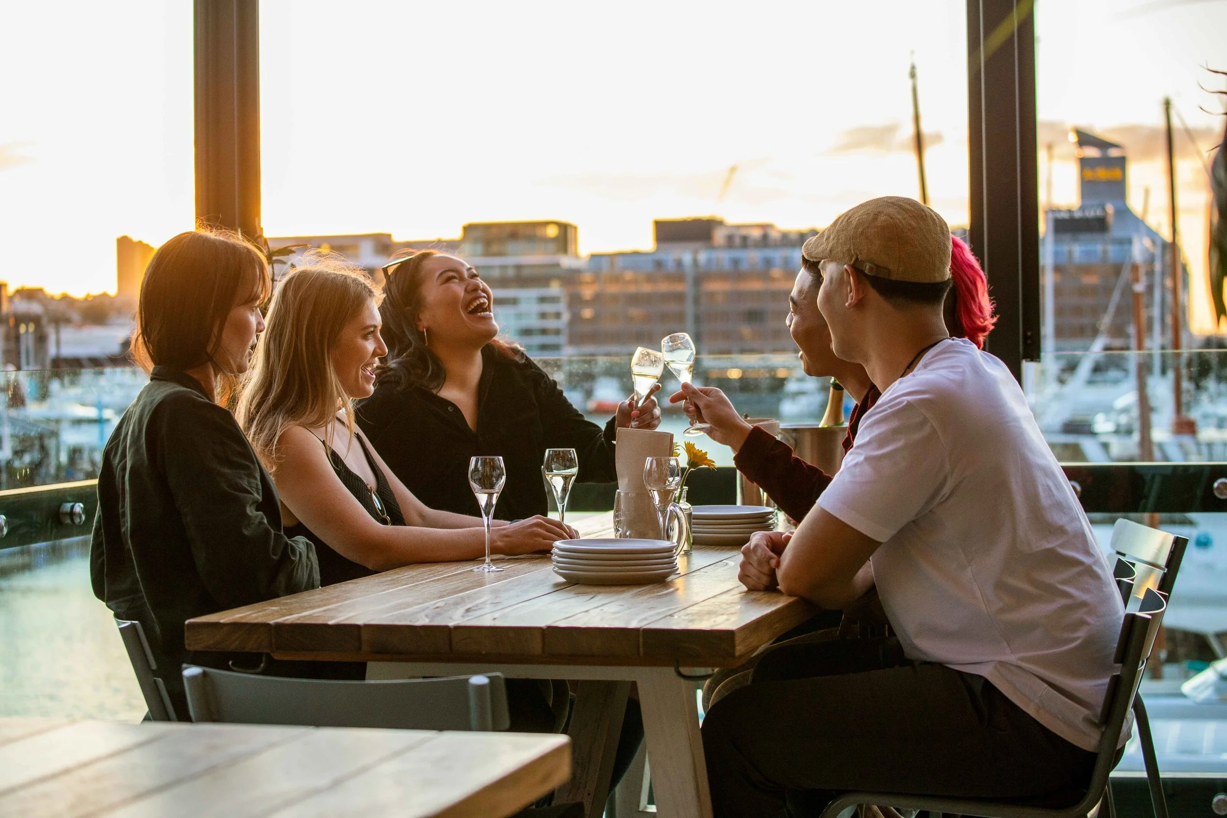 A group of people enjoys wine and a meal together for waterfront dining at the Viaduct Harbour in New Zealand, with scenic views of the water and surrounding landscape