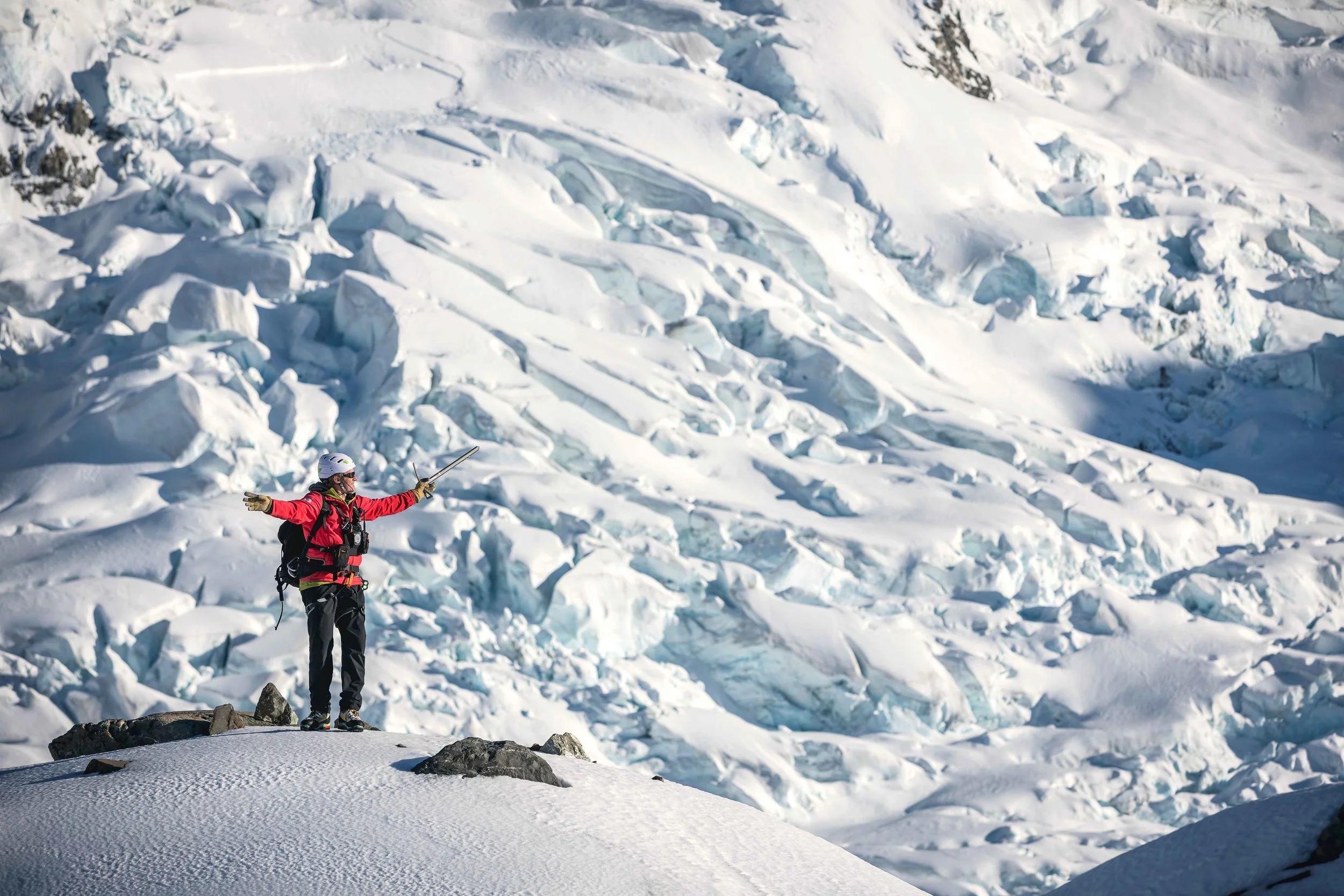 A person stands on a rocky lookout at Aoraki/Mount Cook in Canterbury, taking in the dramatic snow-covered peaks and alpine landscape