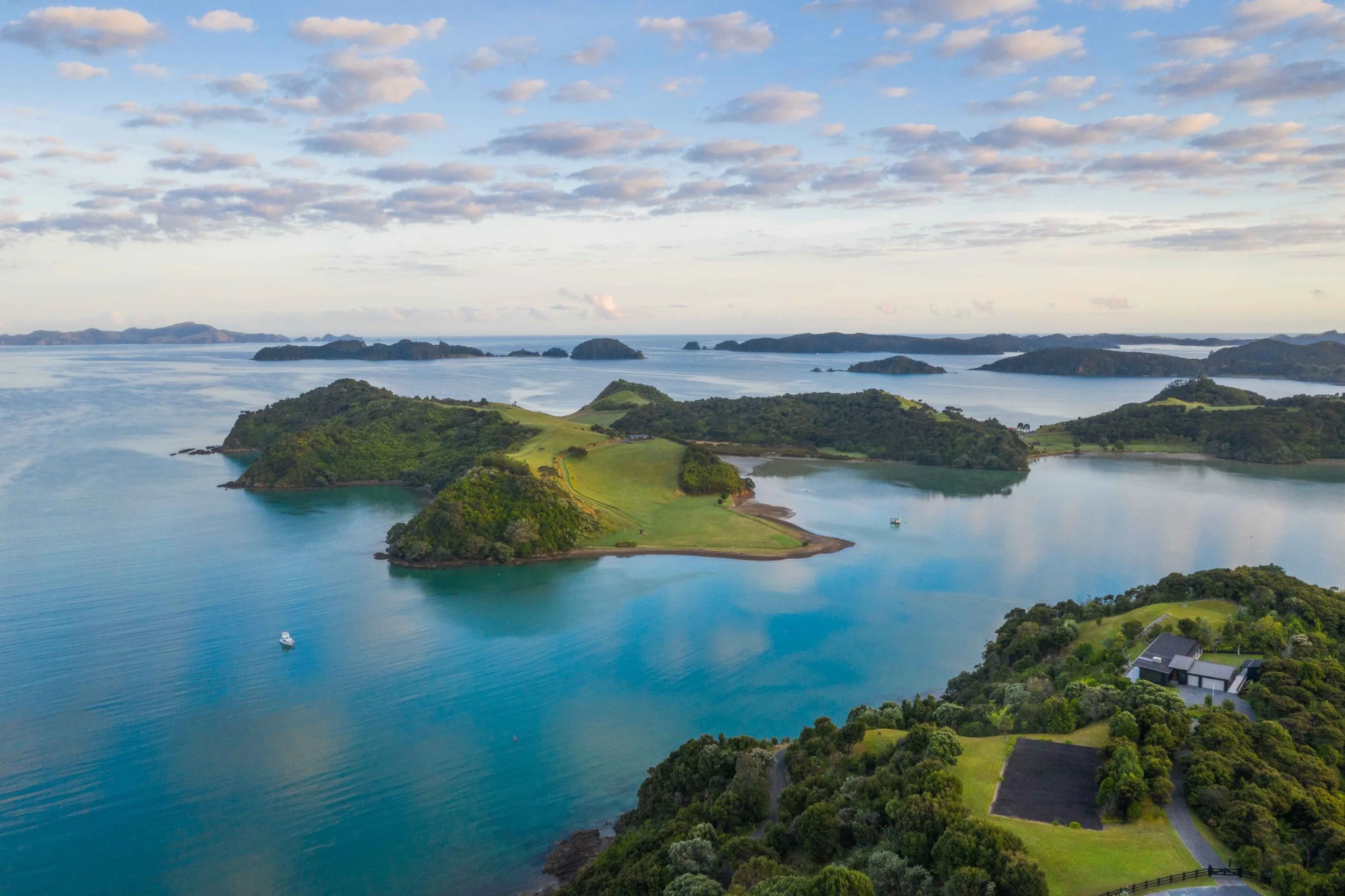 A scenic view of the Bay of Islands in New Zealand, featuring calm blue waters, scattered islands, and lush green coastlines