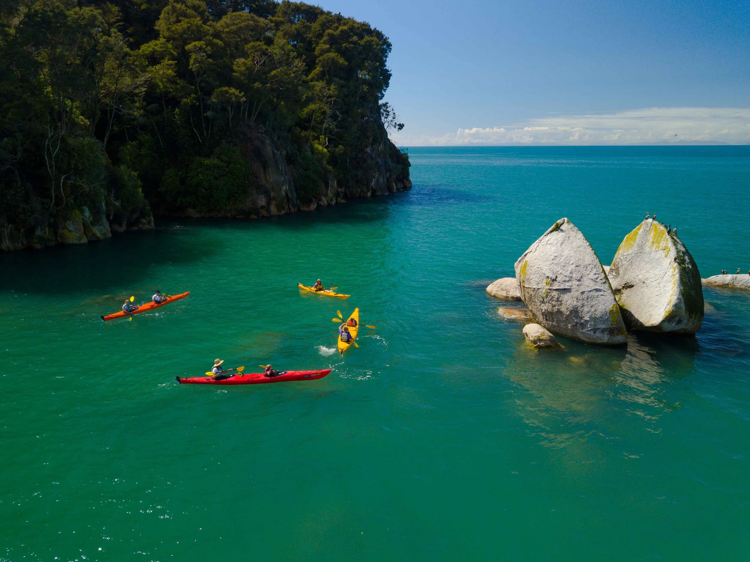 People kayak through green waters around Split Apple Rock near Abel Tasman National Park in Nelson, New Zealand