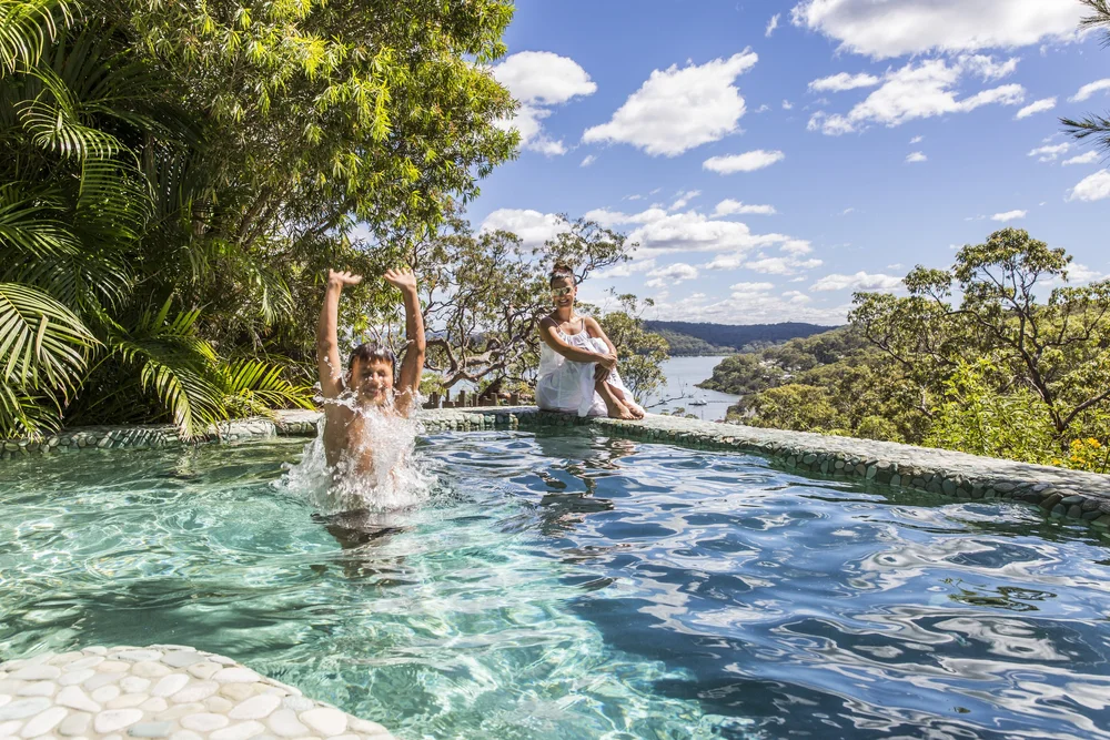 A woman sitting poolside at the Pretty Beach House in Australia while a child plays in the water.