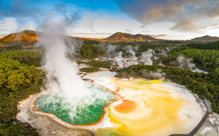 Aerial footage of hot sulphur springs at sunrise, showing a geothermal reserve of boiling water and steam evaporating in a place on the North Island of New Zealand called Rotorua.