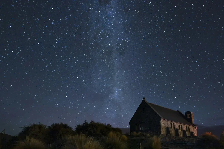 A dark house with a sloped roof and a chimney against a starry night sky, with the Milky Way visible.