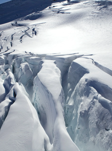 A snowy mountain landscape with large ice and snow formations and a helicopter with a few people on the snow nearby.