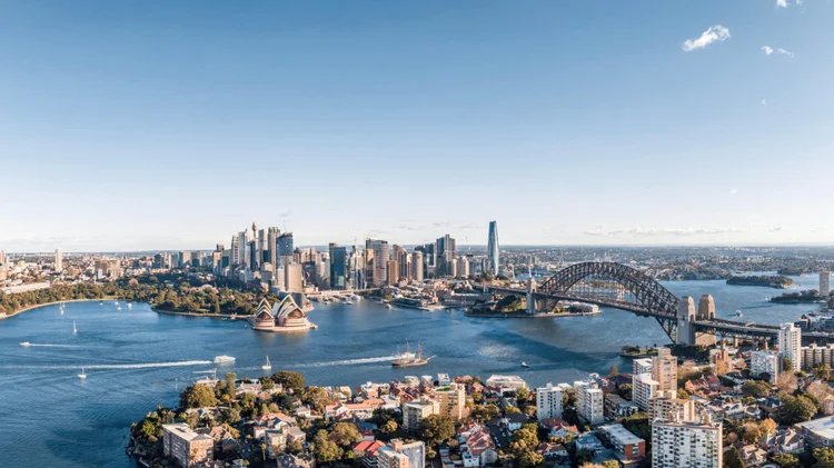 Aerial view of Sydney, Australia highlighting the Sydney Opera House, Sydney Harbour Bridge, and the city skyline with boats on the harbor on a clear day.