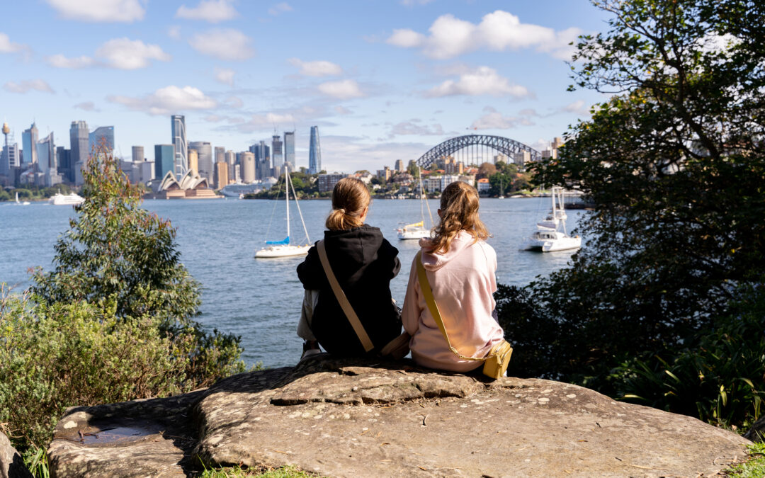 Two young girls are enjoying a beautiful view of the Sydney Opera House, Harbour Bridge, and the city skyline from Cremorne Point.