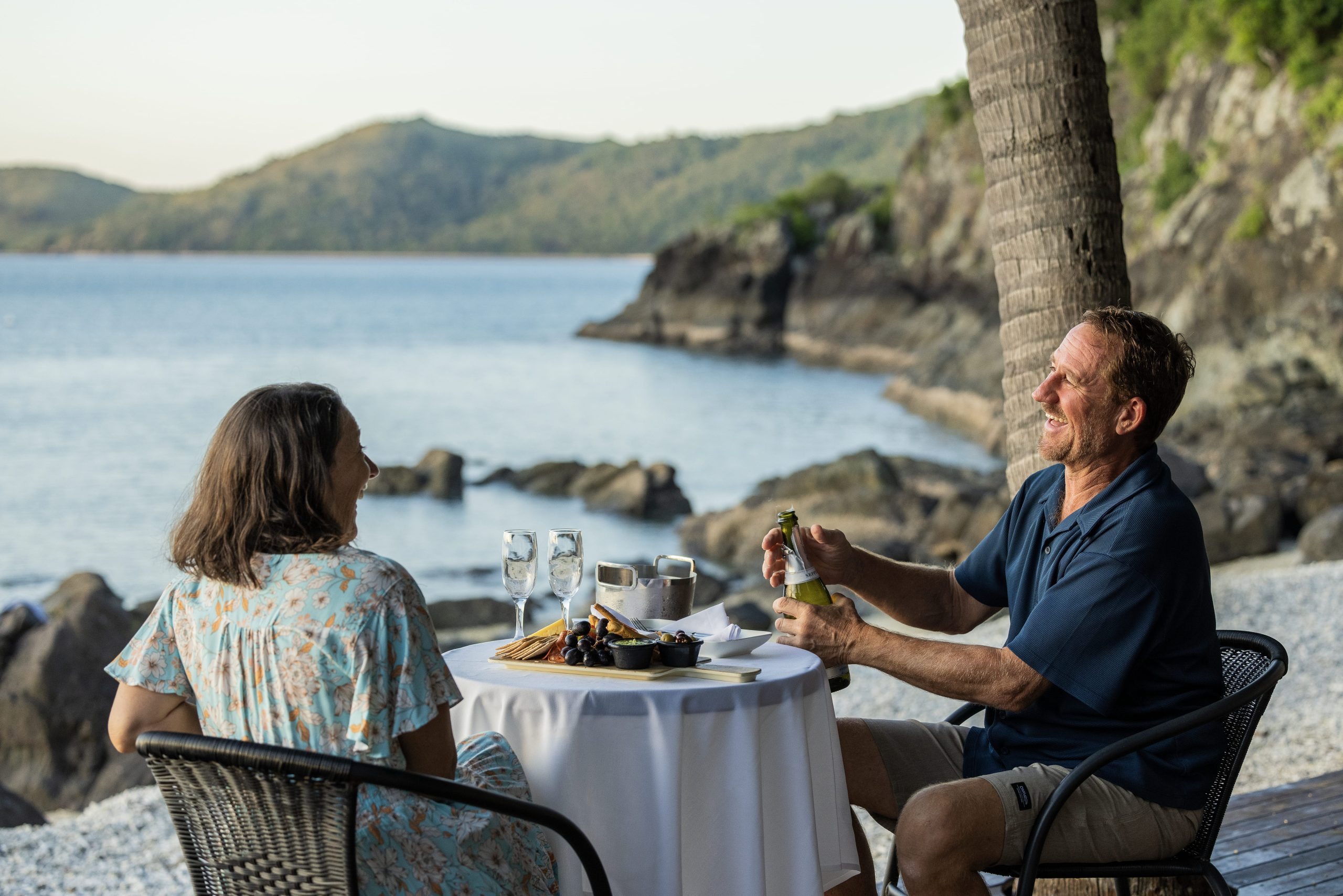 Happy couple opens a bottle of wine while enjoying charcuterie on Australian coast.